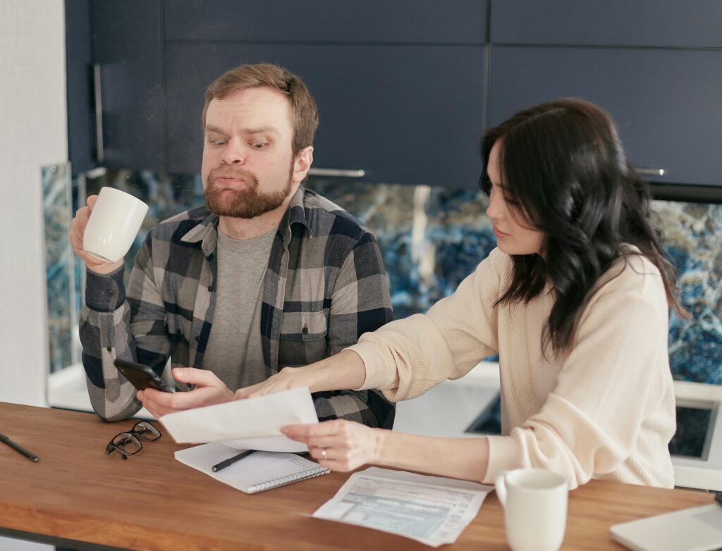 Homeowners seated at a table concerned with unforeseen repair costs due to the poor work of an unlicensed imposter contractor.