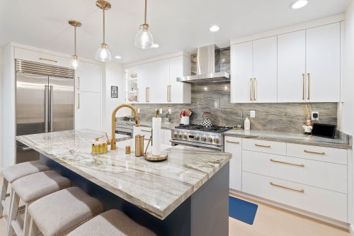 Ed Neir Construction Remodeled kitchen with Sub-zero frig, quartzite countertops + backsplash, custom white + navy cabinets, gold fixtures, pendant/ceiling/in-cabinet lighting.