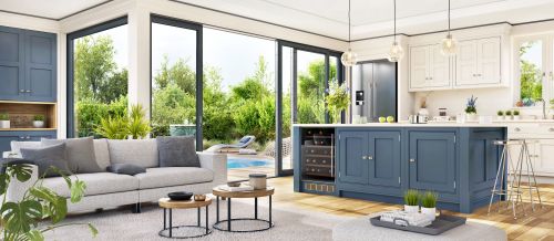 Ed Neir Construction integrates indoor/outdoor kitchens: clean white & navy custom cabinets, island, pendant lighting + large sliding glass window leading to patio seating & pool.
